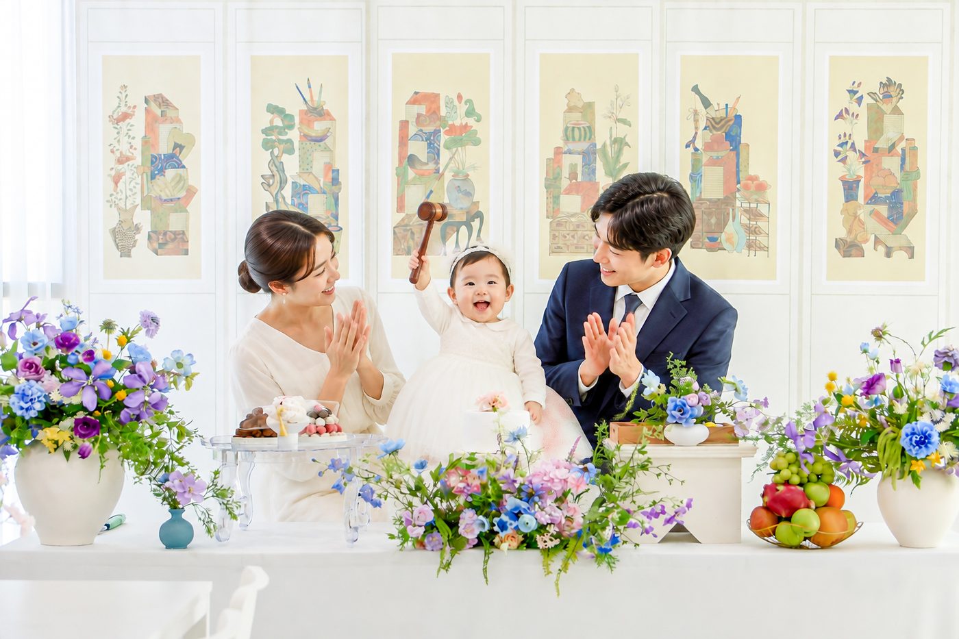 돌잡이 방망이를 든 아기와 박수 치는 부모, 꽃장식된 돌상